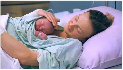 Mãe e bebê em pele a pele na golden hour após o parto.